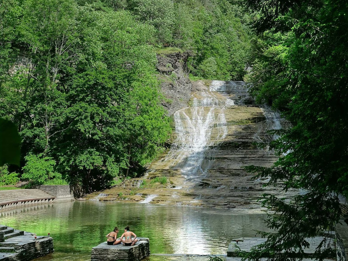 Two people sitting by a waterfall and swimming area